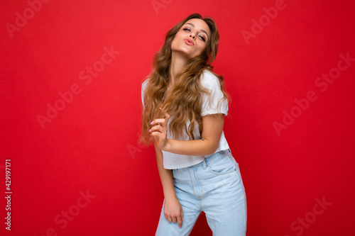 Young beautiful curly blonde woman with sexy expression, cheerful and happy face wearing casual white t-shirt isolated over red background with copy space