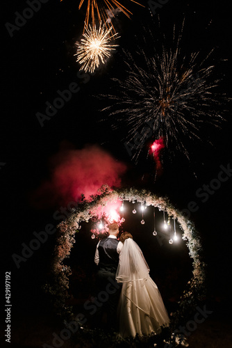 Wedding day of the bride and groom, night vows near the arch with lights on the background of fireworks