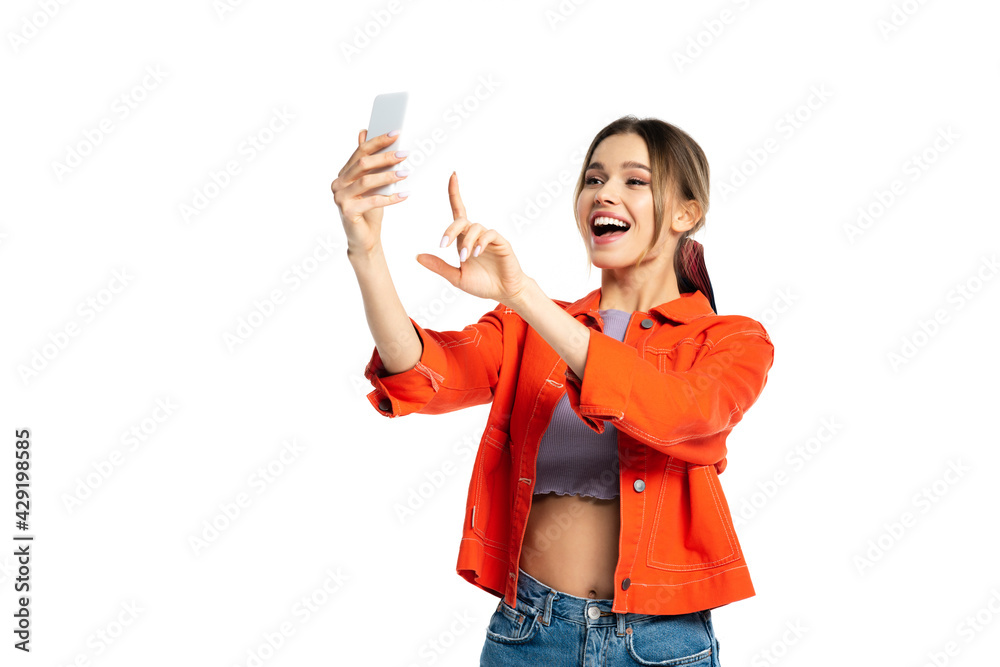 amazed young woman in crop top and orange shirt taking selfie on smartphone and gesturing isolated on white amazed young woman in crop top and orange shirt taking selfie on smartphone and gesturing isolated on white