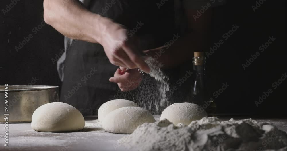 Chef prepares dough for traditional Italian pizza. Cooker sprinkles flour on dough in kitchen, 4k footage