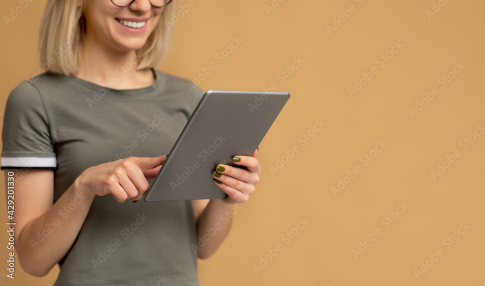 Unrecognizable young woman with newest digital tablet standing on beige studio background with empty space Unrecognizable young woman with newest digital tablet standing on beige studio background with empty space