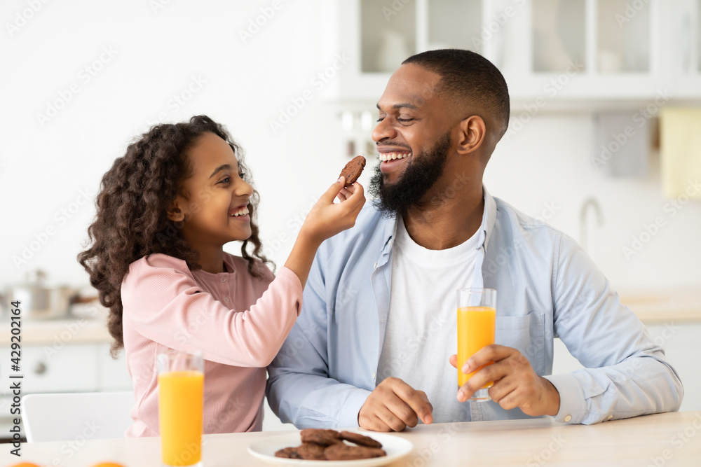 Cheerful african american girl feeding dad with cookie Cheerful african american girl feeding dad with cookie