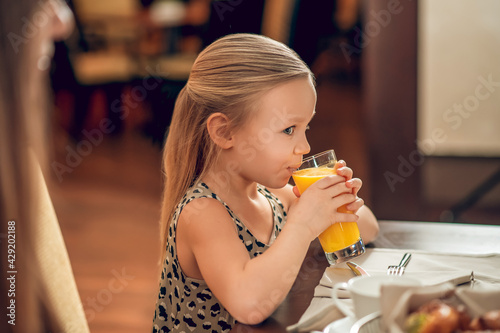 Cute girl sitting at the table and drinking orange juice