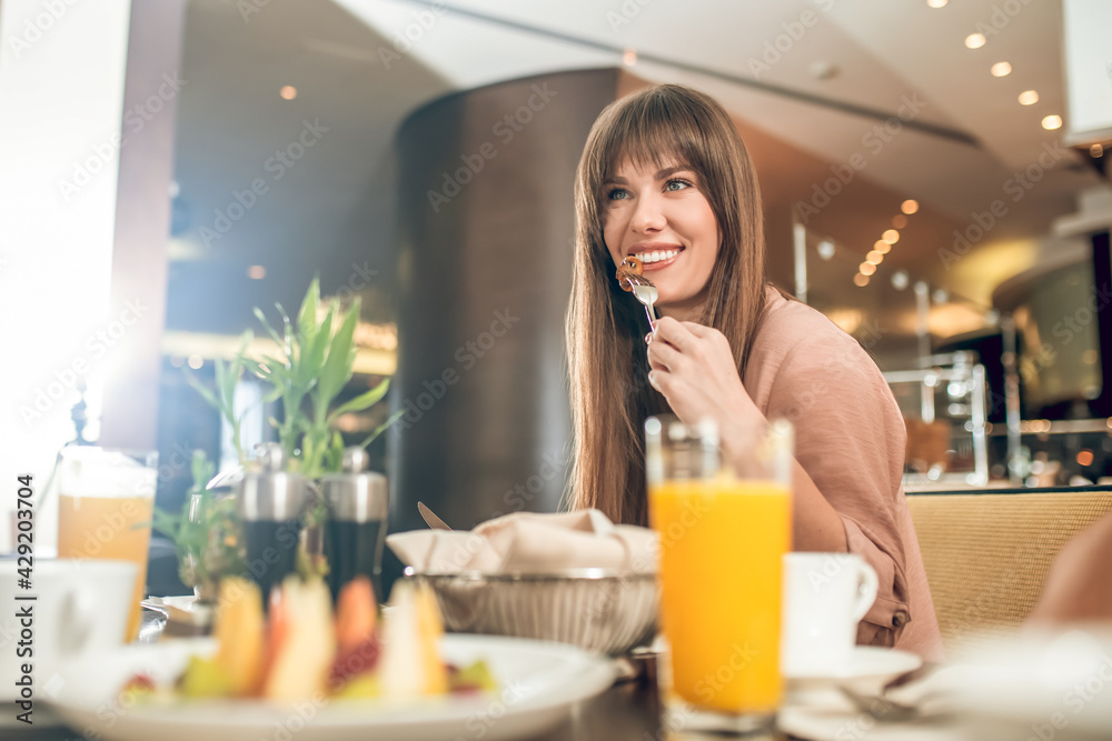 Long-haired young woman having breakfast and looking contented Long-haired young woman having breakfast and looking contented