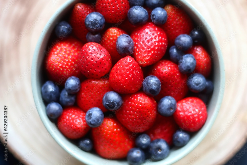 Bowl of blueberries and strawberries on wooden tray. Flat lay, dark textile background.