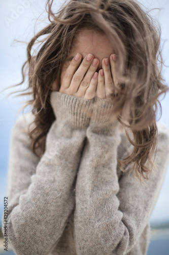 portrait of a beautiful sensual young woman, hair develops the wind, brunette with emotions, hands hair and face, seaside wind outside