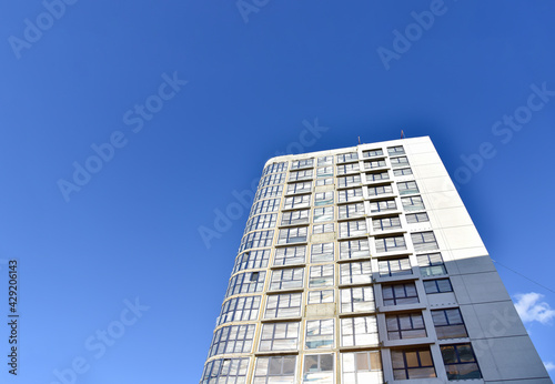 Facade of a new modern high-rise residential building. Skyscraper on blue sky background. Tall house renovation project, government programs. Minimalistic multi storied home.