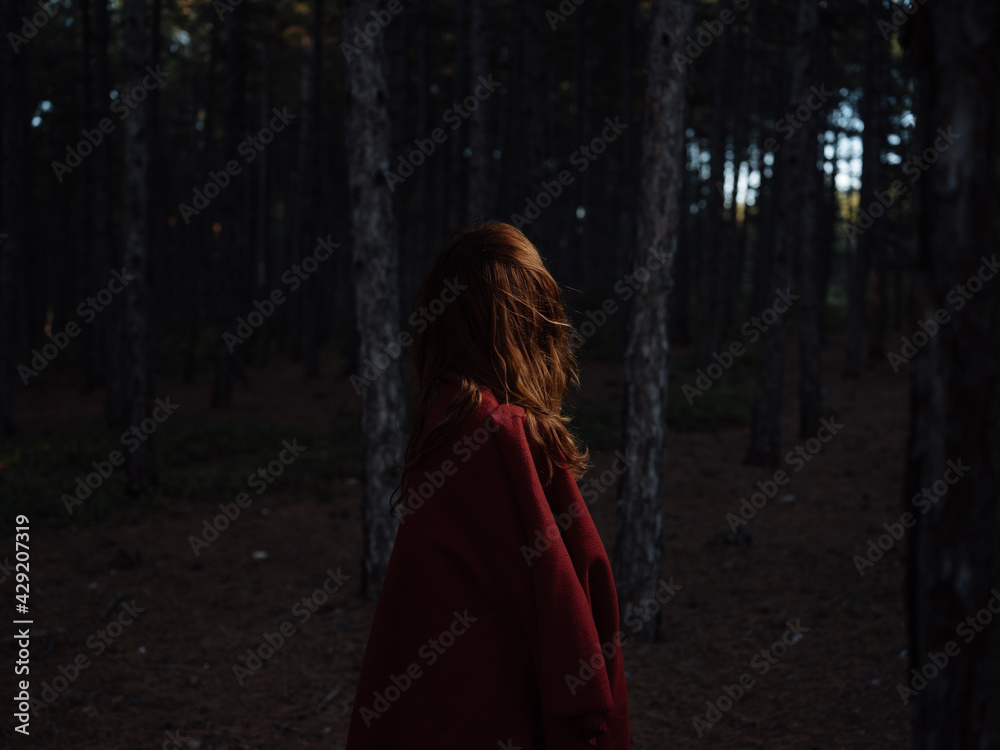 A woman travels in the forest at night with a red plaid on her shoulders, back view A woman travels in the forest at night with a red plaid on her shoulders, back view