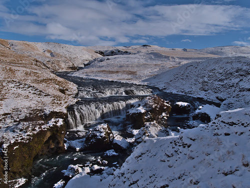 Beautiful view of water cascades of Skógá river near Fimmvörðuháls trail in rocky canyon surrounded by snow-covered meadows on sunny winter day near Skógá village on the southern coast of Iceland.