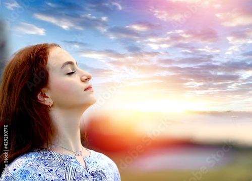 Banner with a young girl holding a bouquet of lilac lupins in her hands, closing her eyes. Enjoying nature and the scent of flowers. Stunning sky and sunset background. Relax. Copy space on the right