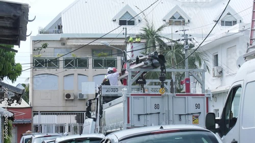 Travaux sur des lignes électriques dans une rue de la Ville de Saint Denis de l'île tropicale de la Réunion, les ouvriers sont dans une nacelle engin de chantier pour faire la réparation 