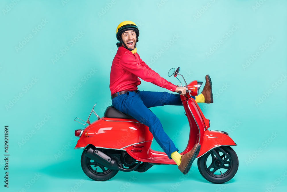 Full length profile side photo of brunette excited man ride motorbike speed isolated on teal color background Full length profile side photo of brunette excited man ride motorbike speed isolated on teal color background