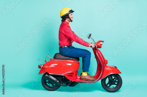 Full size profile side photo of charming happy young man ride motorcycle wear helmet isolated on teal color background