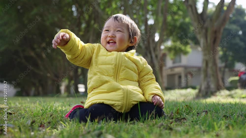 happy little asian girl in yellow coat sitting on the spring meadow outdoor in the sunny park happy little asian girl in yellow coat sitting on the spring meadow outdoor in the sunny park
