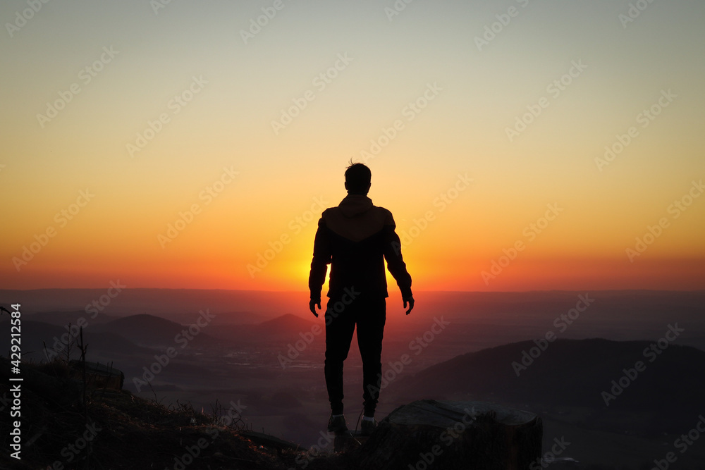 Silhouette of a young athlete who stands on a tree stump and is surrounded by a pounding ball of the setting sun. Add confidence. Ondrejnik, Beskydy mountains, czech republic
