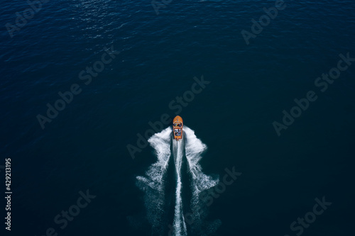 Classic Italian motor boat. Top view of a wooden boat sailing to the blue sea. Wooden runabout in the rays of the sun on blue water. Drone view of a boat the blue clear waters.