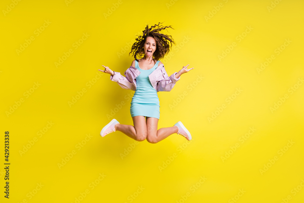 Full size photo of happy funky funny crazy girl jumping showing tongue rock'n'roll sign isolated on yellow color background Full size photo of happy funky funny crazy girl jumping showing tongue rock'n'roll sign isolated on yellow color background