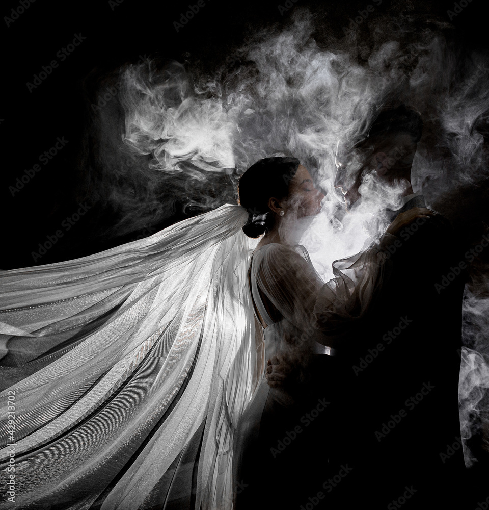 Side view of newlyweds hugging and looking at each other in the smoke on a black background. Concept of wedding couple Side view of newlyweds hugging and looking at each other in the smoke on a black background. Concept of wedding couple