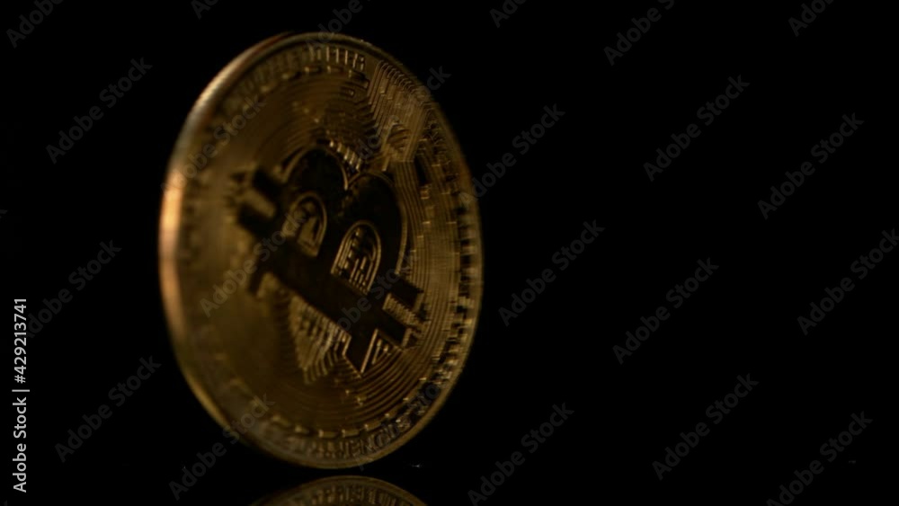 Close up one golden bitcoin physical coin spins over black background, super slow motion Close up one golden bitcoin physical coin spins over black background, super slow motion