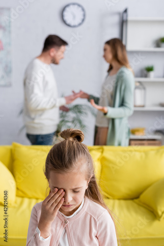 Daughter crying near parents having conflict on blurred background.