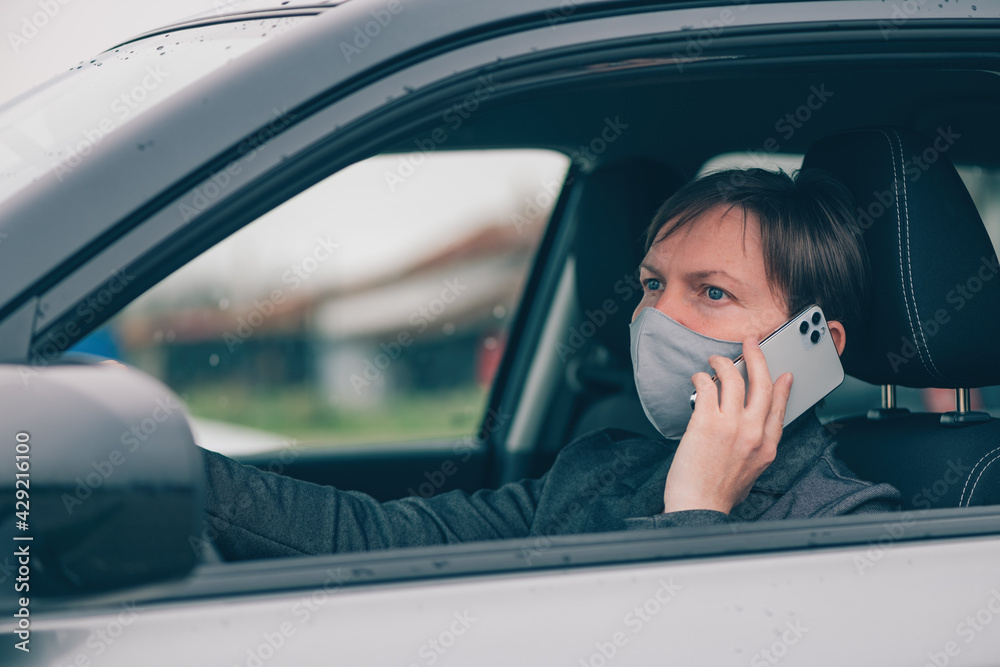Woman with protective face mask talking on mobile phone from her car during Covid-19 pandemics Woman with protective face mask talking on mobile phone from her car during Covid-19 pandemics