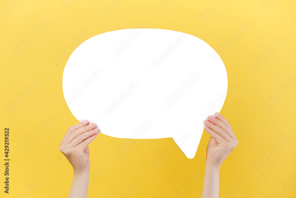 Close up of female hands holding an empty white paper speech bubble, isolated over pastel yellow studio background wall with copy space for advertisement. Dialog concept - obrazy, fototapety, plakaty 