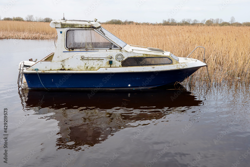 Obraz premium Old worn small fishing boat on a calm water in a lake. Cloudy sky. Nobody. Small river vessel. Hobby and transportation concept