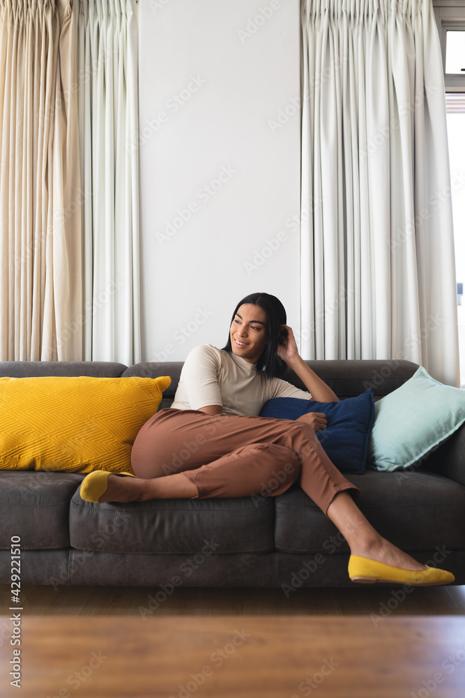 Happy mixed race transgender woman relaxing in living room sitting on couch smiling Happy mixed race transgender woman relaxing in living room sitting on couch smiling