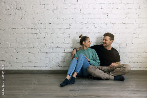 young happy couple sitting on the floor by the wall in empty apartment room. moving to new home concept. copy space
