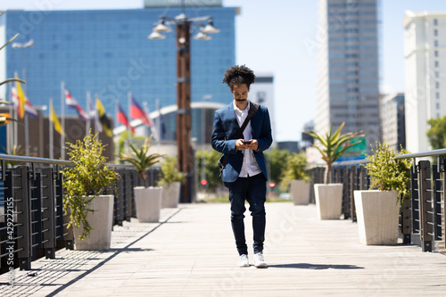 Smartly dressed mixed race man with moustache walking on street using smartphone photo