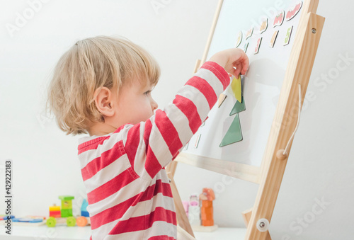 Obraz na płótnie Cute little child playing at a magnetic board, learning letters, numbers and geometric shapes at home. Educative and funny indoor activity for early development. w salonie