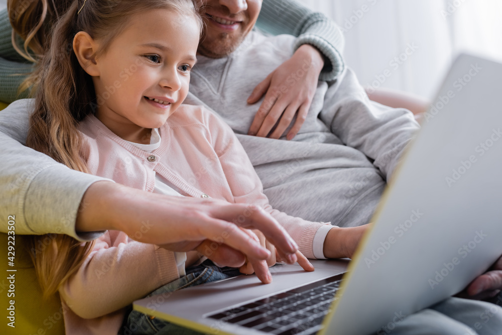 Smiling child using laptop near parents on blurred background.