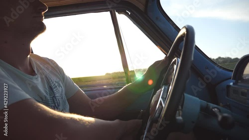 Wallpaper Mural Low angle view of caucasian man in hat holding hands on steering wheel and driving a retro car at sunset. Silhouette of guy traveling in a vintage vehicle at countryside. Slow motion Close up Torontodigital.ca