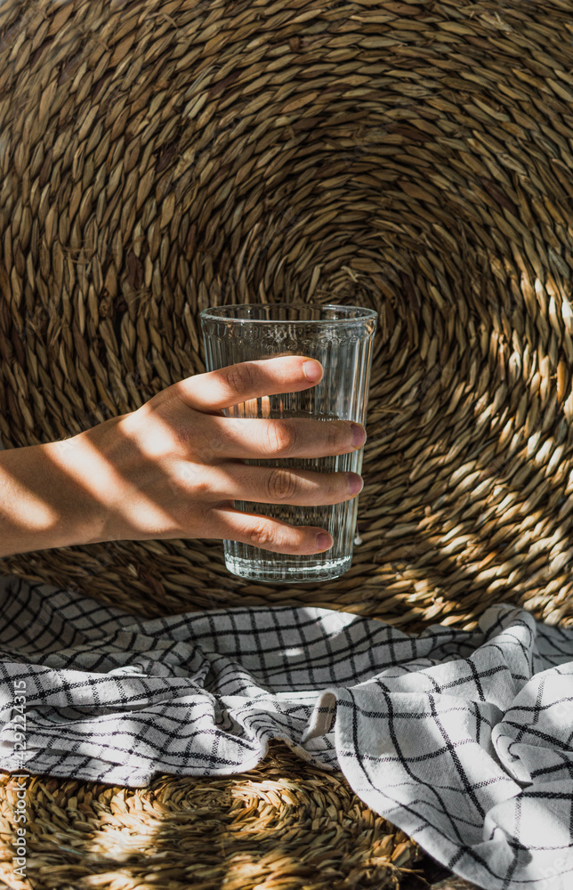 Mano femenina sujetando un vaso de cristal transparente y textura estriada.  El vaso, medio lleno de