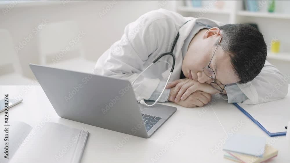 Exhausted doctor sleeping at office desk, tired of extra hours shift in hospital Exhausted doctor sleeping at office desk, tired of extra hours shift in hospital