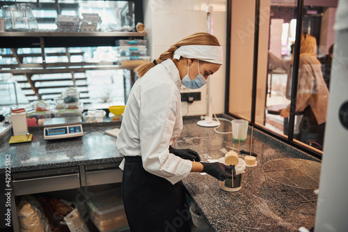 Responsible woman in chef uniform and mask making desserts