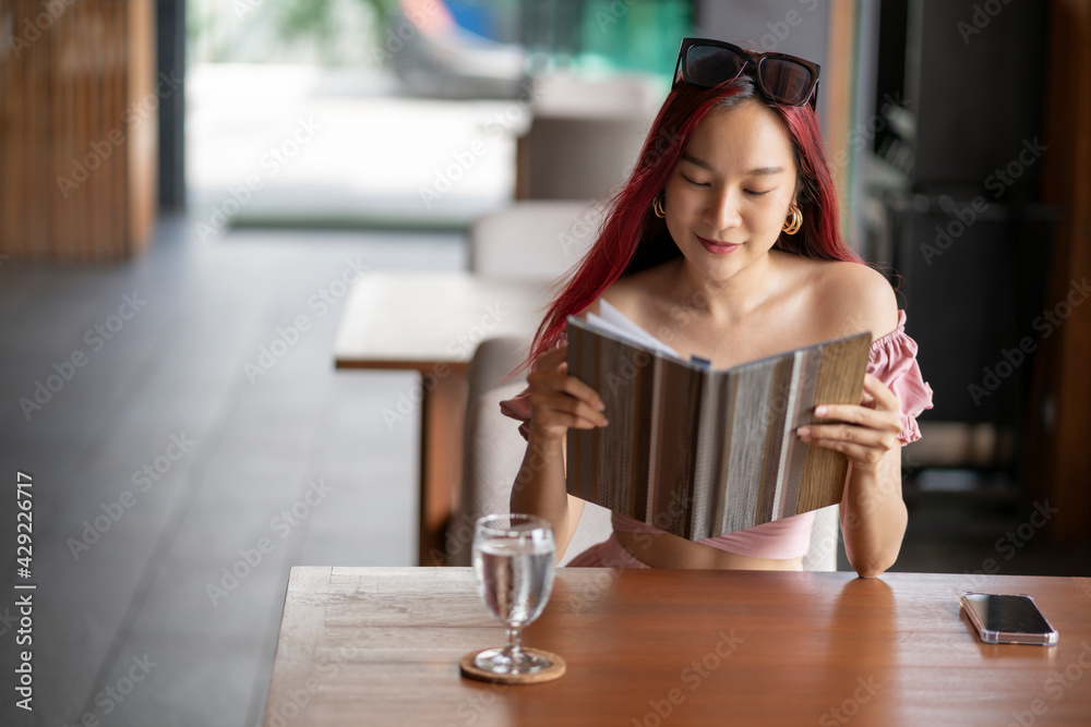 Young Asian woman reading and choosing menu in hotel restaurant on her vacation day. travel lifestyle concept Young Asian woman reading and choosing menu in hotel restaurant on her vacation day. travel lifestyle concept