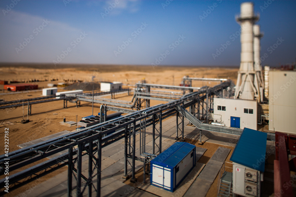 Kzylorda region/Kazakhstan - May 01 2012: Modern gas power plant in desert. Blurred picture with tilt-shift effect. Pipeline in focus. Dark sky and yellow sand background.