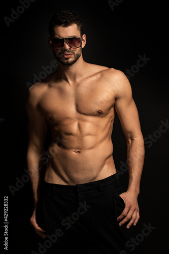 Muscle strong beautiful stripped male model in black trousers wearing glasses eyewear on black isolated font background