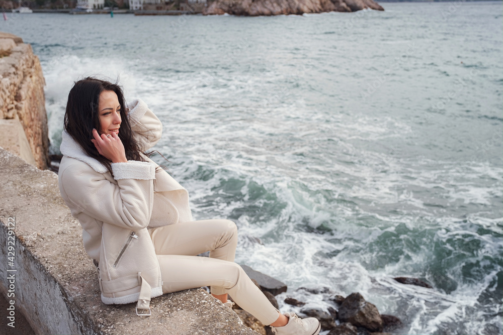 A woman in beige clothing enjoying the view of the sea on a warm, windy day.