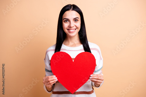 Photo of young happy lovely positive cheerful smiling girl hold big red heart isolated on beige color background