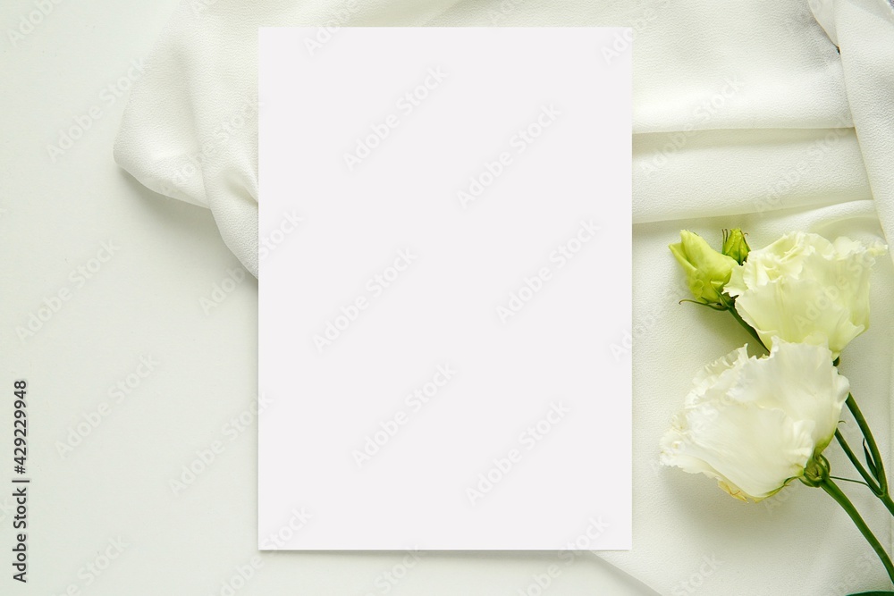 Wedding stationery mockup, white blank vertical card for design presentation, flat lay composition with white flowers and bride dress.