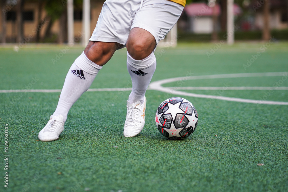 Bangkok, Thailand - April 2021: A football player who is wear Asics  football shoe in white color is training dribbling ball on local turf  pitch. Selective focus. Stock Photo | Adobe Stock