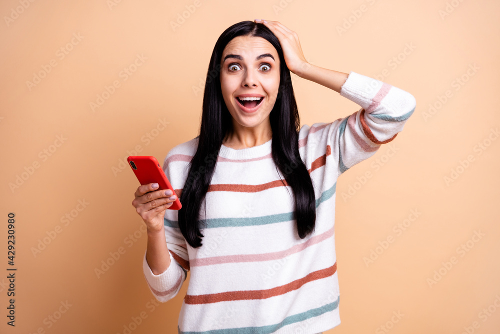 Photo of young crazy woman happy smile amazed shocked surprised use cellphone hand touch head isolated over beige color background Photo of young crazy woman happy smile amazed shocked surprised use cellphone hand touch head isolated over beige color background