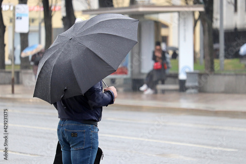 Heavy rain in city, man with umbrella standing on road background. Rainy weather, spring storm