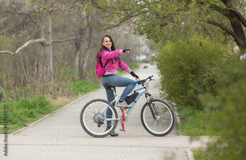 a sporty girl rides a bicycle on a pedestrian path , she saw something or someone, or teases, points with her hand