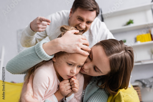 Woman covering frightened kid near irritated husband on blurred background.