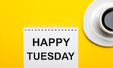 On a bright yellow background, a white cup with coffee and a white notepad with the words HAPPY TUESDAY