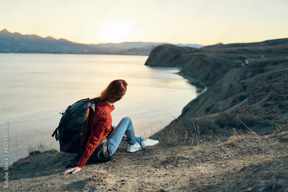 a traveler with a backpack looks at the sunset at the sea in the mountains