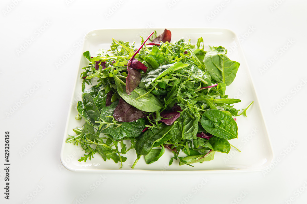 salad mix of fresh herbs, arugula, chard, spinach in a plate on a white plate, top-side view salad mix of fresh herbs, arugula, chard, spinach in a plate on a white plate, top-side view